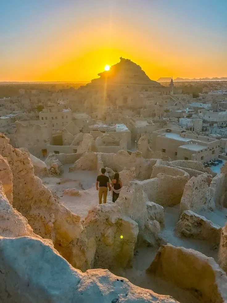 Viajeros contemplando las ruinas de adobe de Shali al atardecer