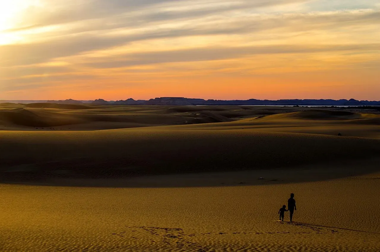 Dos viajeros cruzando las dunas de Siwa al atardecer